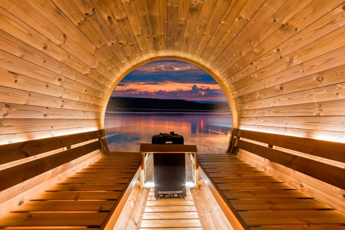 ハルビア バレルサウナのフルムーンの室内。奥が全面ガラスになっていて、夕暮れの湖が正面いっぱいに広がる。中央にハルビアのヒーター（写真：HARVIA）