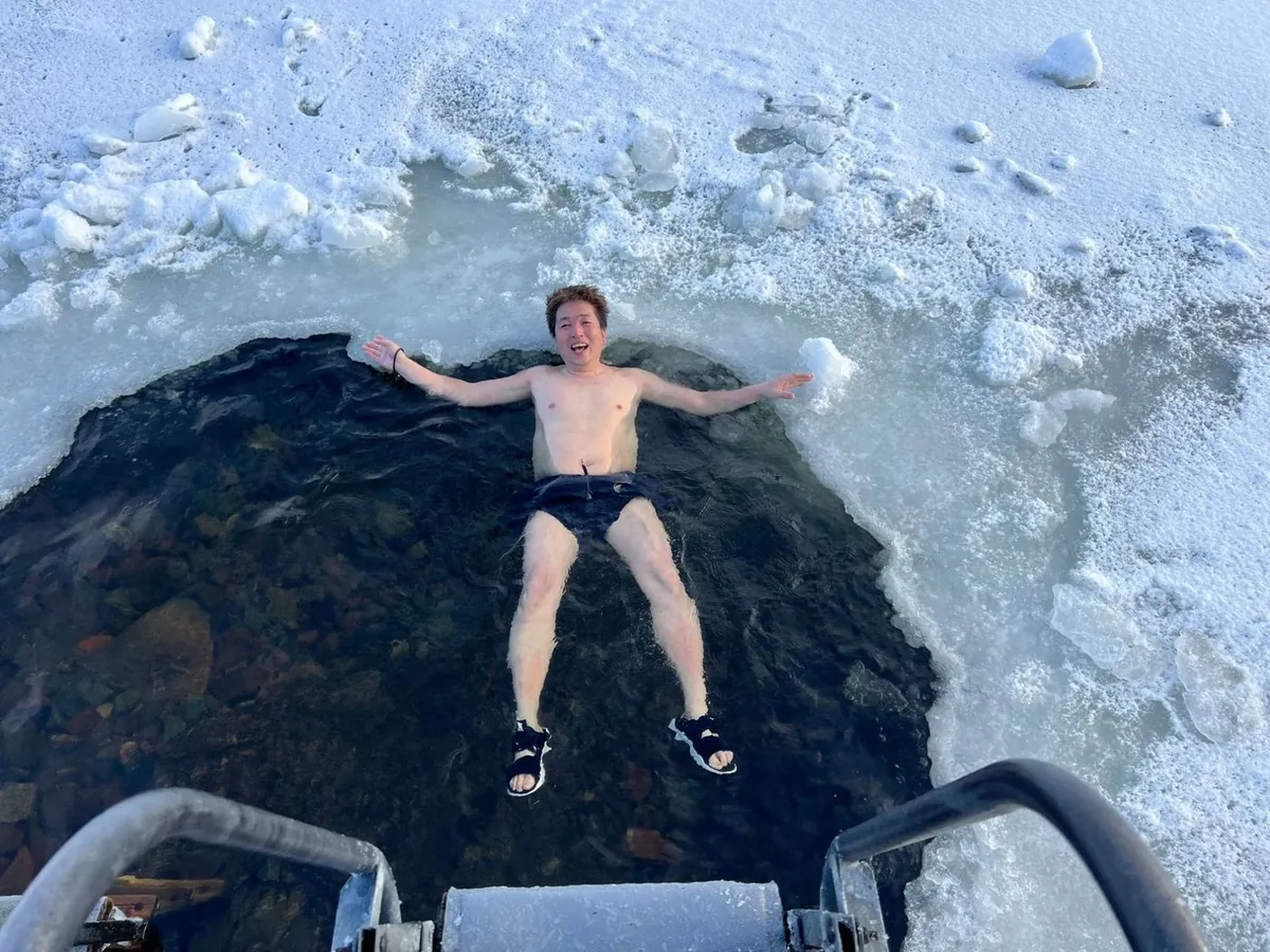 はしごの先、氷の穴に仰向けで浮かぶ水着の男性