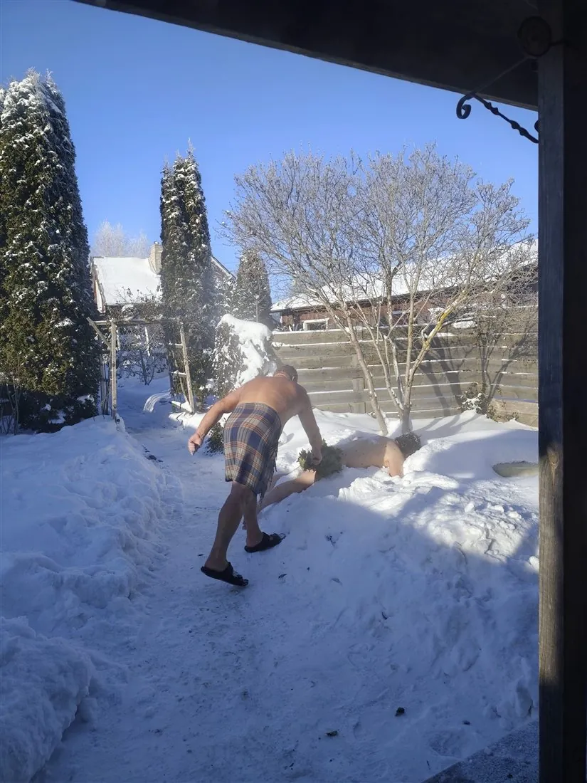 雪の庭で、寝そべる人に葉の束を当てる様子