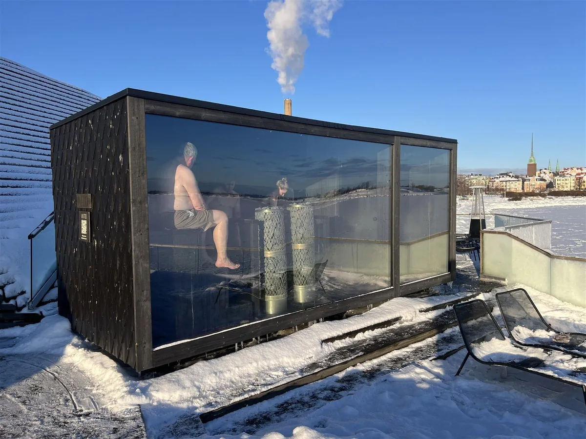 雪の上に建つガラス張りのサウナ小屋と、中で座る人