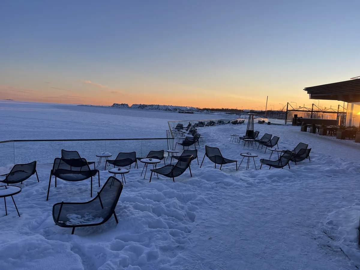 雪のテラスに並ぶ椅子と、凍った海の夕焼け