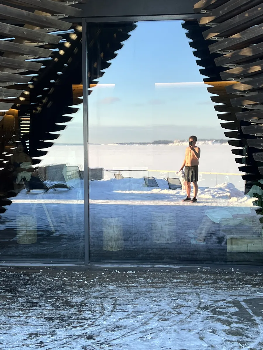 雪のデッキから見た大きなガラス窓。凍った海と水着の人が映り込む