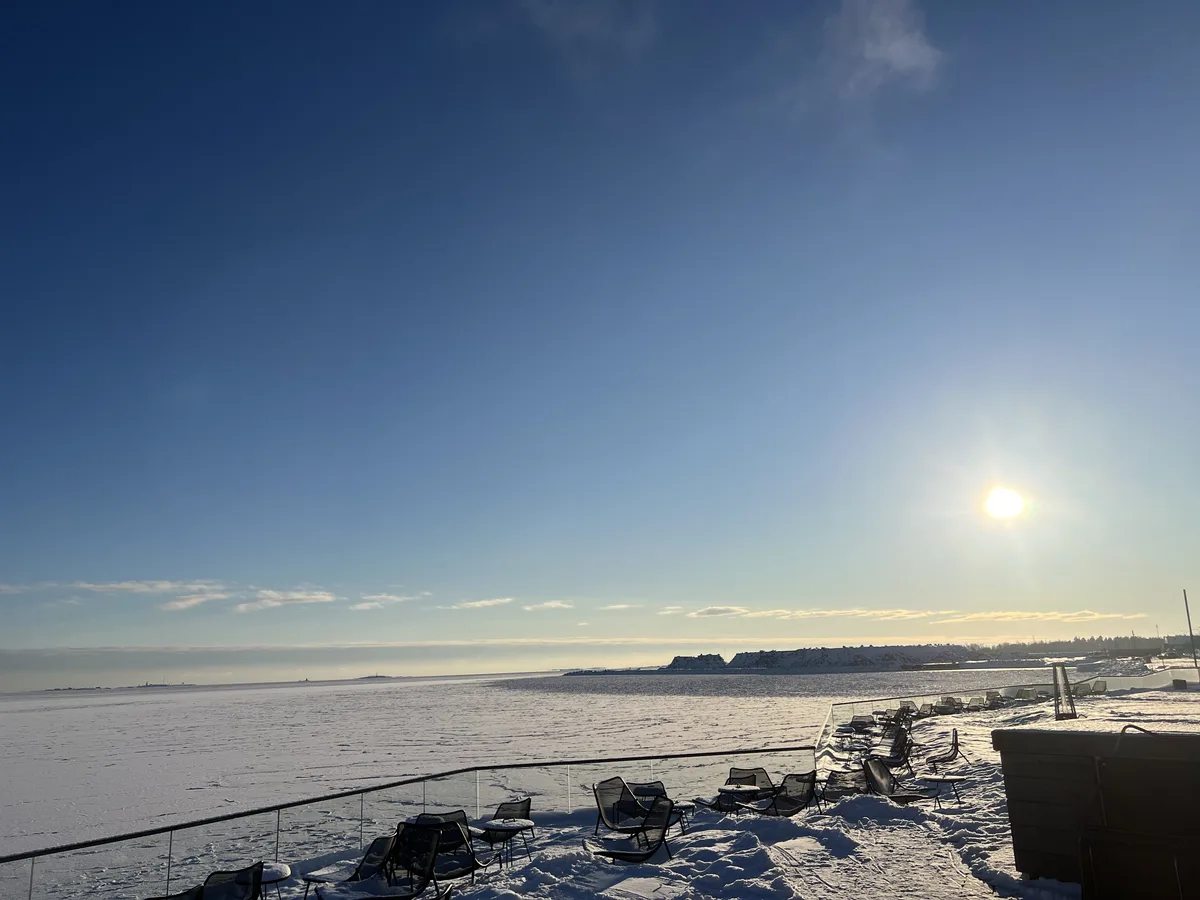 雪の積もったテラスに並ぶ椅子と、凍った海に低く照る冬の太陽