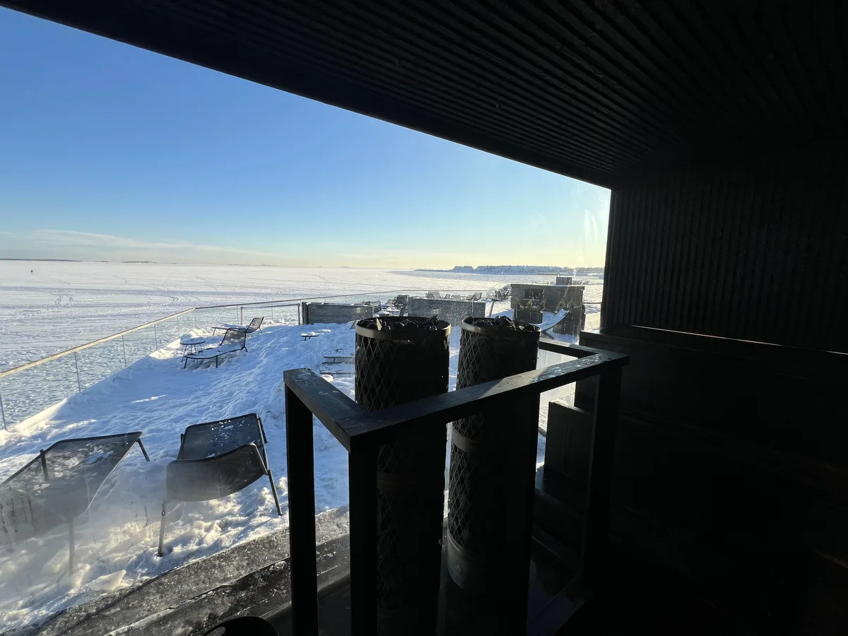サウナ室の窓から見た雪のテラスと凍った海、手前にストーブ2基