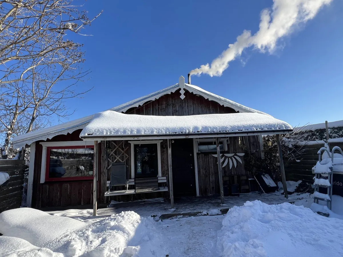 雪の積もった赤茶色の木造小屋と煙突の煙